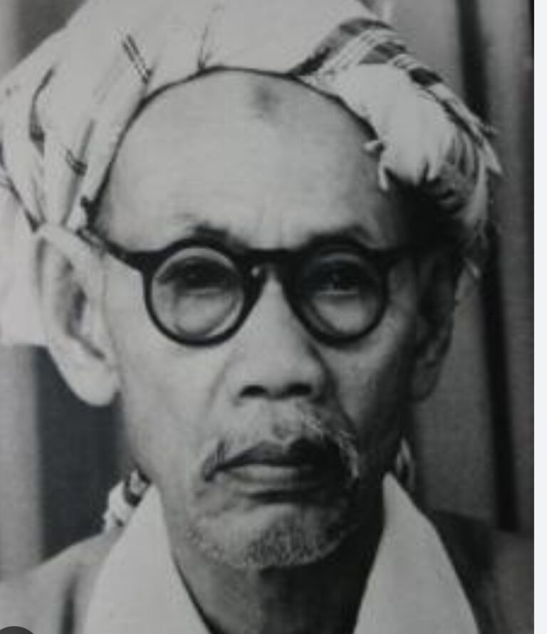 Portrait of Mahatma Gandhi wearing round glasses and a cloth on his head, looking thoughtful.